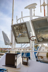 A mast of a boat, featuring large deck floodlights and a marine radar scanner. The floodlights are...