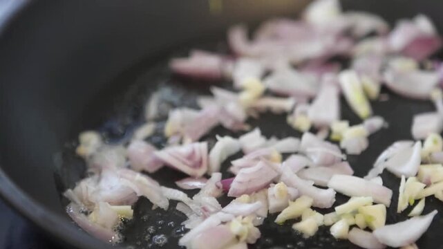 Chopped onions and garlic are being fried in a pan with oil for a tasty dish