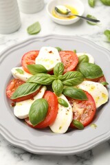 Tasty salad Caprese with mozzarella, tomatoes, basil and spices on white marble table, closeup