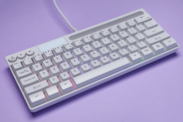 White keyboard with RGB lighting on violet background, closeup