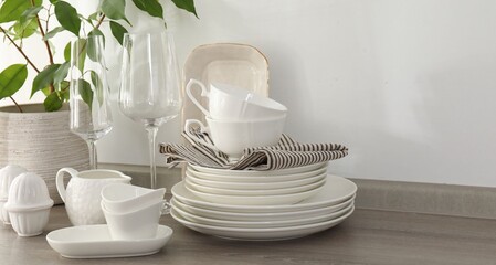 Different clean white dishware, glasses and houseplant on counter in kitchen, closeup
