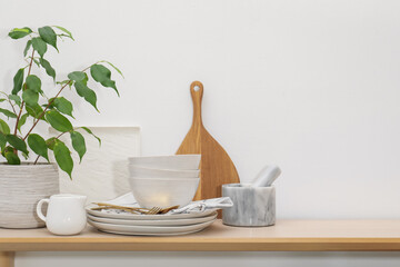 Different clean white dishware, cutlery, cutting board and floral decor on wooden table indoors, space for text