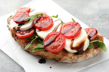 Delicious sandwich with mozzarella cheese, balsamic sauce, tomato and arugula on grey table, closeup