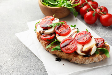 Delicious sandwich with mozzarella cheese, balsamic sauce, tomatoes and arugula on grey table, closeup. Space for text