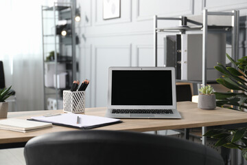 Stylish workplace with laptop, stationery and floral decor on wooden table in office