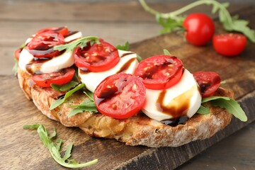 Delicious sandwich with mozzarella cheese, balsamic sauce, tomatoes and arugula on wooden table, closeup