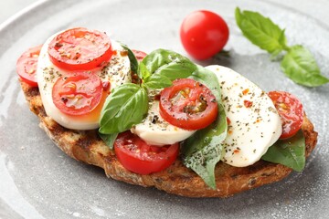 Delicious sandwich with mozzarella cheese, tomatoes and basil on plate, closeup