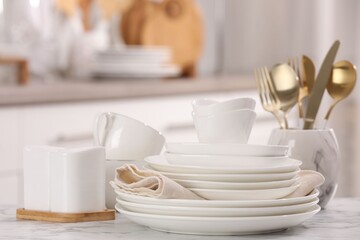 Different clean white dishware, cups and cutlery on marble table indoors, closeup