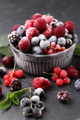 Mix of ripe frozen berries, mint leaves and bowl on dark textured table, closeup
