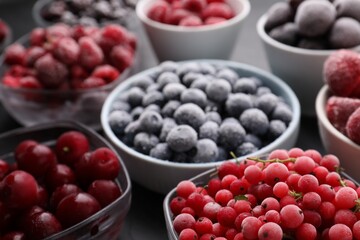 Different ripe frozen berries in bowls on grey table, closeup
