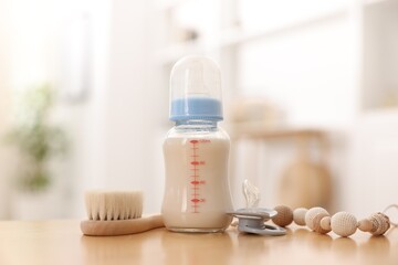 Bottle with milk and baby accessories on table indoors