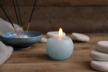 Burning candle, spa stones and incense sticks on wooden table, closeup