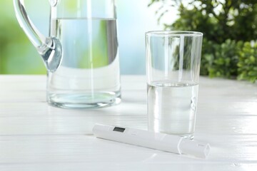 Nitrate tester and glass of water on white wooden table, closeup