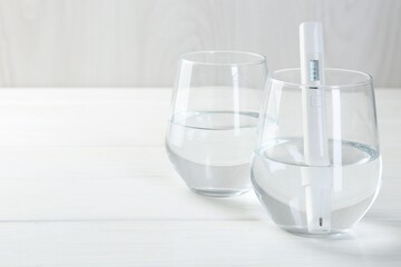 Nitrate tester in glass of water on white wooden table, closeup. Space for text
