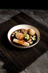 Assorted pempek Palembang served in dark cuko vinegar sauce with diced cucumber. Traditional Indonesian fishcakes in a bowl—great for menus, recipes, or culinary features.