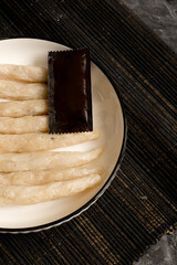 Close-up of uncooked pempek lenjer on a plate with a blank chili sauce packet. Ingredient concept...