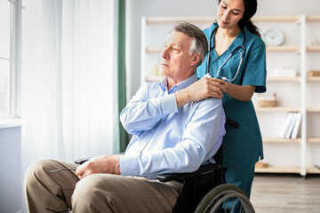 Young doctor holding elderly disabled male's hand, giving him support at retirement home. Senior...