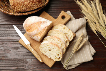 Fresh bread, knife and wheat spikes on wooden table, flat lay