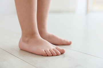 Little girl standing barefoot on warm floor indoors, closeup. Heating system