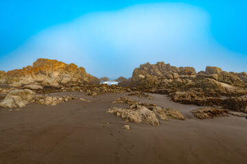 A close-up of large rock formations and tide pools on the shore of Matanzas, Chile, under a misty,...