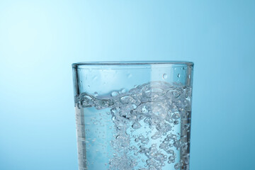 Refreshing soda water in glass against light blue gradient background, closeup