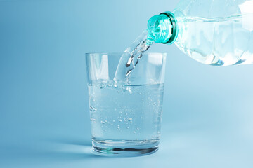 Pouring refreshing soda water from bottle into glass on light blue gradient background, closeup