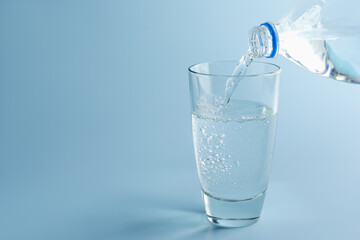 Pouring refreshing soda water from bottle into glass on light blue gradient background, closeup....