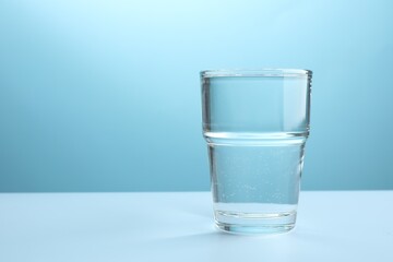 Refreshing soda water in glass on white table against light blue gradient background, closeup. Space for text