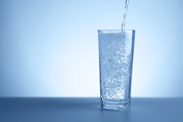 Pouring refreshing soda water into glass at table against light blue gradient background, closeup. Space for text