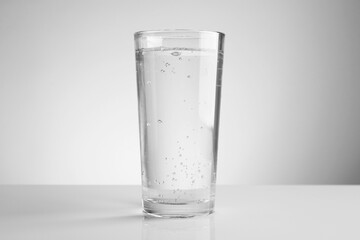 Refreshing soda water in glass on light mirror table against grey gradient background, closeup