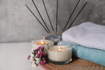 Spa composition with burning candles on white wooden table near grey wall, closeup. Space for text