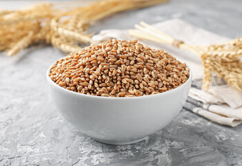 Wheat grains in bowl and spikes on grey table, closeup