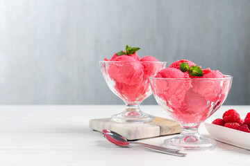 Delicious raspberry sorbet with mint in dessert bowls, spoons and fresh berries on white wooden...