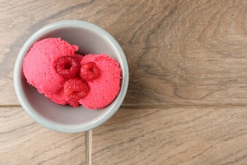 Delicious raspberry sorbet with fresh berries in bowl on wooden table, top view. Space for text