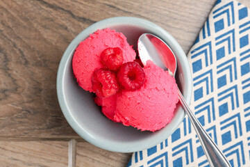 Delicious raspberry sorbet with fresh berries and spoon in bowl on wooden table, top view