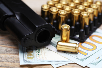 Metal bullets, gun and dollars on wooden table, closeup
