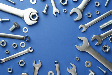 Metal wrenches, nuts and bolts on blue background, flat lay. Space for text