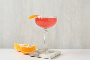 Martini cocktail with garnish and slices of orange on white table