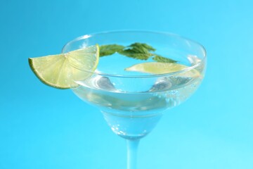 Martini cocktail with slices of lime and mint on light blue background, closeup