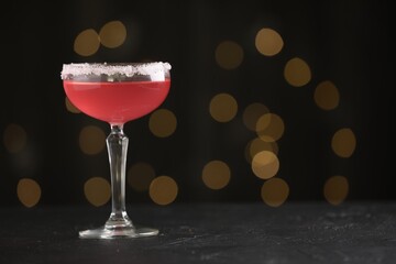 Martini cocktail with sugar in glass on black table against blurred lights, closeup. Space for text