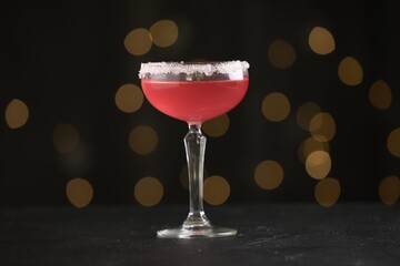 Martini cocktail with sugar in glass on black table against blurred lights, closeup