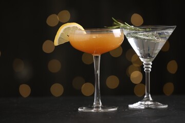 Different martini cocktails in glasses on black table against blurred lights, closeup. Space for text