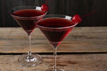 Martini cocktail with cherries in glasses on wooden table, closeup