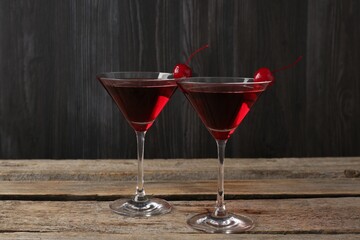 Martini cocktail with cherries in glasses on wooden table, closeup