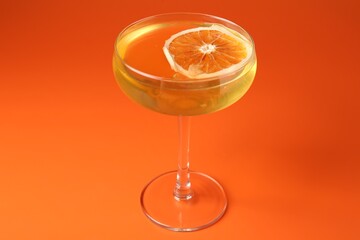 Martini cocktail with orange slice in glass on orange background, closeup
