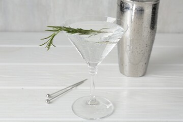 Martini cocktail with rosemary in glass and shaker on white wooden table, closeup