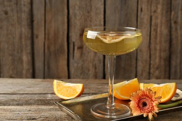 Martini cocktail in glass, orange slices and flower on wooden table, closeup. Space for text