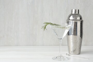 Martini cocktail with rosemary in glass and shaker on white wooden table, closeup. Space for text