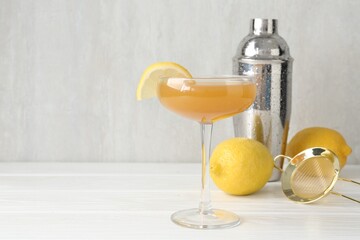 Martini cocktail with lemon slice in glass, fruits and shaker on white wooden table, closeup. Space...