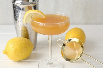Martini cocktail with lemon slice in glass, fruits and shaker on white wooden table, closeup
